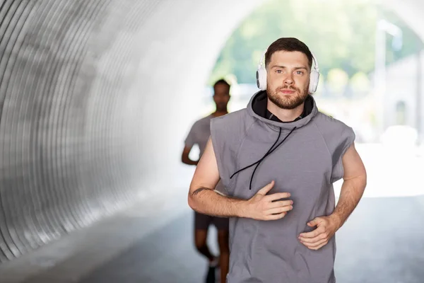 Male friends with headphones running outdoors — Stock Photo, Image
