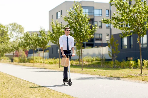 Affärsman med lunch i papperspåse Riding Scooter Stockfoto