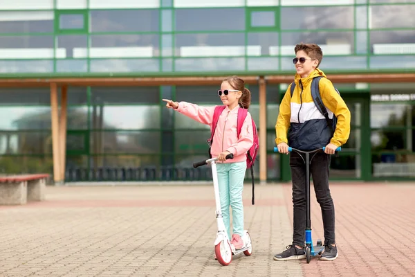Gelukkige schoolkinderen met rugzakken en scooters — Stockfoto