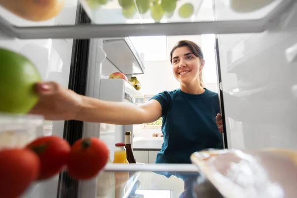 Счастливая женщина принимает еду из холодильника дома — стоковое фото