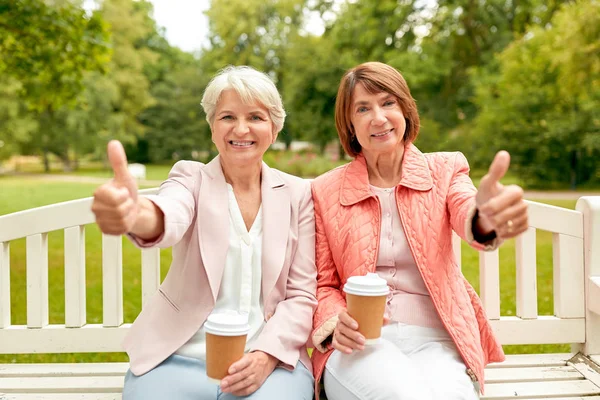 Donne anziane con caffè mostrando pollici al parco — Foto Stock