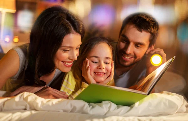 Glückliche Familie liest Buch nachts zu Hause im Bett — Stockfoto