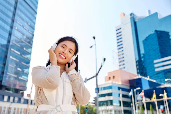 Glad leende asiatisk kvinna med hörlurar i staden — Stockfoto