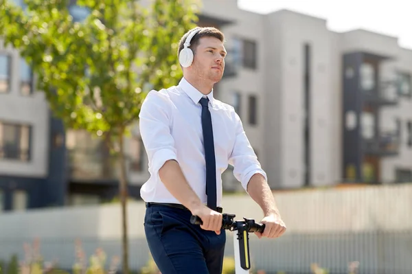 Hombre de negocios con auriculares scooter en la ciudad — Foto de Stock