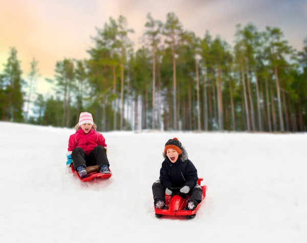 Gelukkig kinderen glijden op sleeën naar beneden heuvel in de winter — Stockfoto