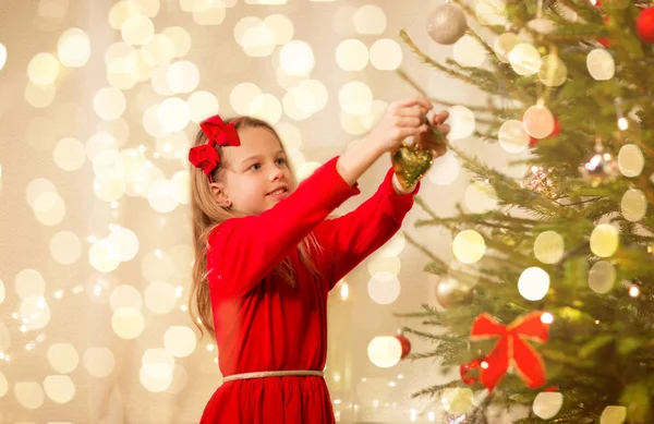 Kırmızı elbiseli mutlu kız Noel ağacı süslüyor. — Stok fotoğraf