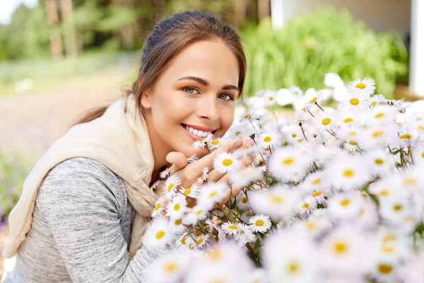 Happy woman smelling chamomile flowers in garden — Stock Photo, Image