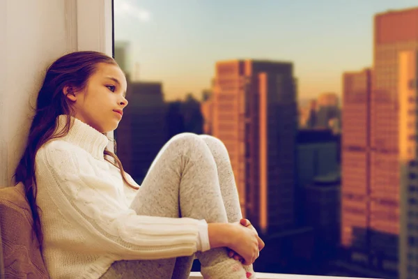 Verdrietig meisje zittend op Sill thuis venster over stad — Stockfoto