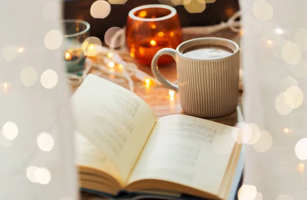 Book and cup of coffee or hot chocolate on table — Stock Photo, Image