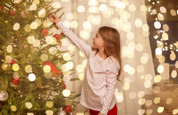 Glückliches Mädchen in rotem Kleid schmückt Weihnachtsbaum — Stockfoto