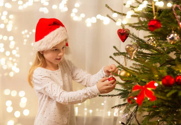 Glückliches Mädchen mit Weihnachtsmütze schmücken Weihnachtsbaum — Stockfoto