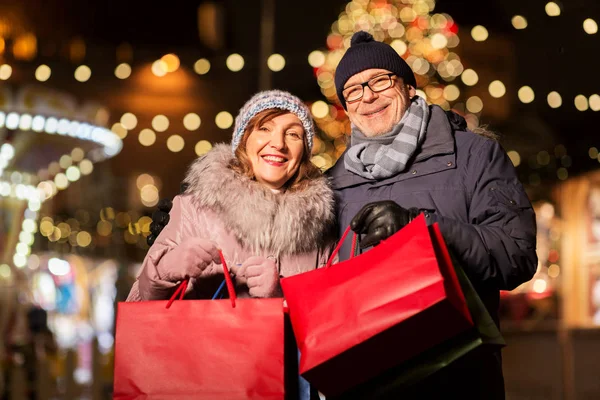 Old couple at christmas market with shopping bags — Stock Photo, Image