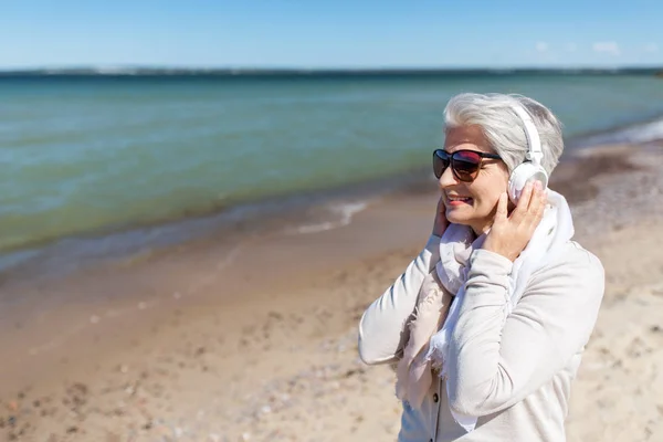 Anciana en auriculares escucha música en la playa —  Fotos de Stock