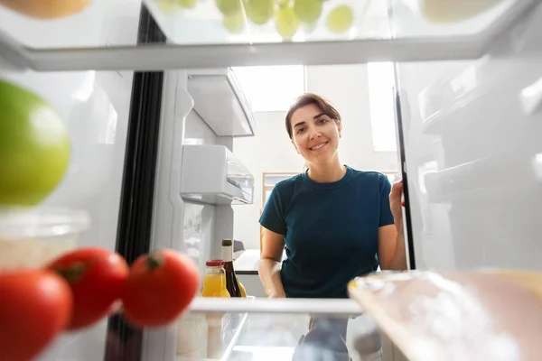 Счастливая женщина у открытого холодильника на домашней кухне — стоковое фото