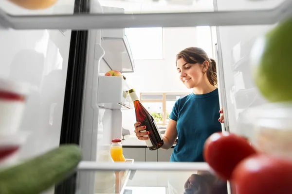 Счастливая женщина берет бутылку вина из холодильника дома — стоковое фото