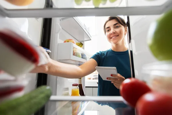 Kvinna gör lista över nödvändig mat hemma kylskåp — Stockfoto