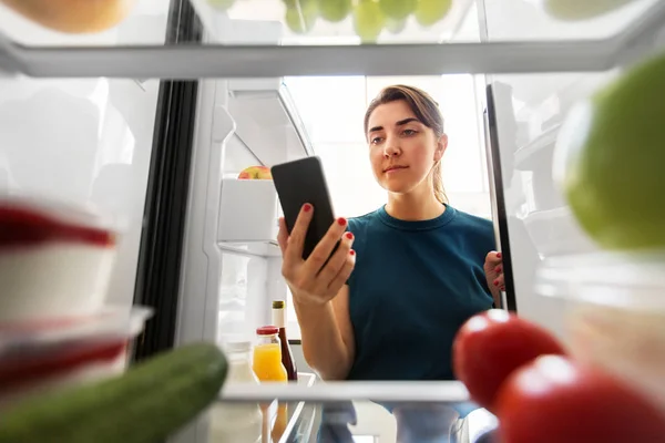 Femme avec smartphone fait la liste des aliments au réfrigérateur — Photo