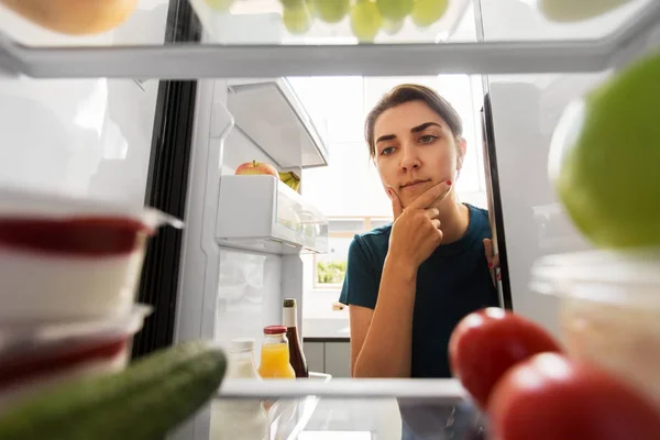 Nachdenkliche Frau am offenen Kühlschrank in der heimischen Küche lizenzfreie Stockbilder