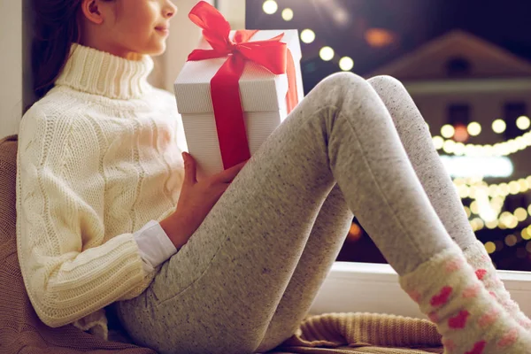 Meisje met kerstcadeau zittend op vensterbank — Stockfoto