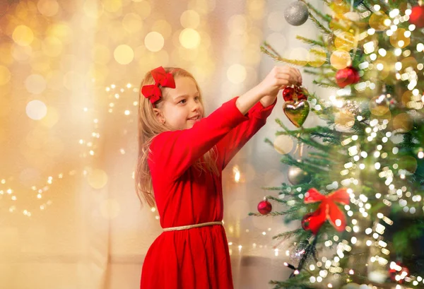 Kırmızı elbiseli mutlu kız Noel ağacı süslüyor. — Stok fotoğraf