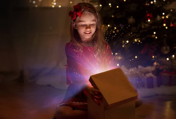 Chica sonriente abriendo regalo de Navidad por la noche Fotos De Stock