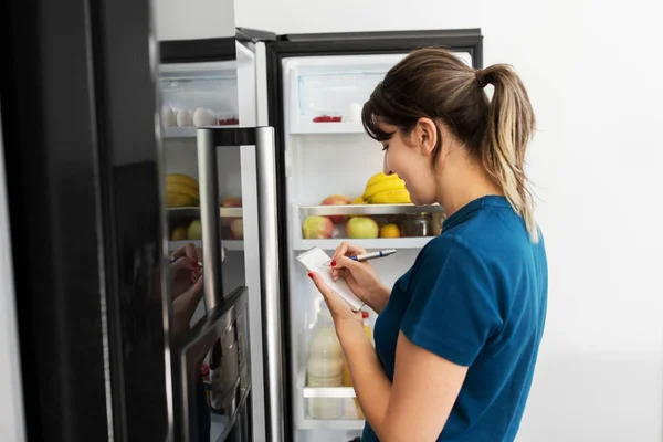 家庭の冷蔵庫で必要な食べ物のリストを作る女性 — ストック写真