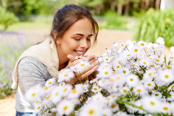 Donna felice profumando fiori di camomilla in giardino — Foto Stock