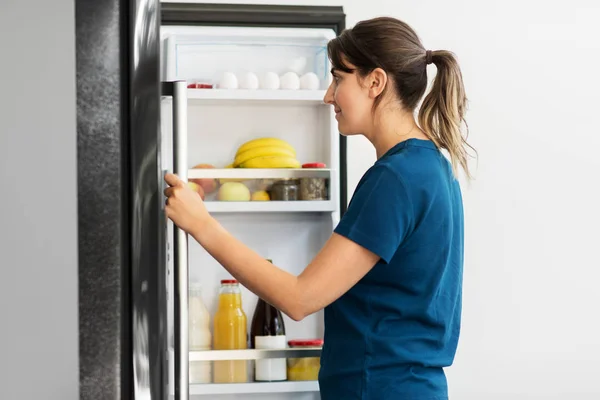 Femme heureuse au réfrigérateur ouvert à la maison cuisine — Photo