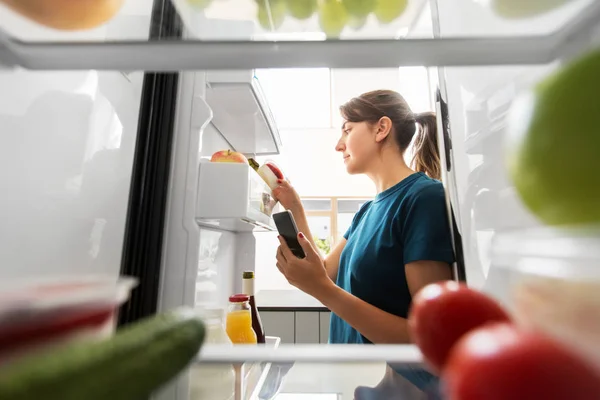 Kvinna med smartphone gör lista över mat i kylskåp — Stockfoto