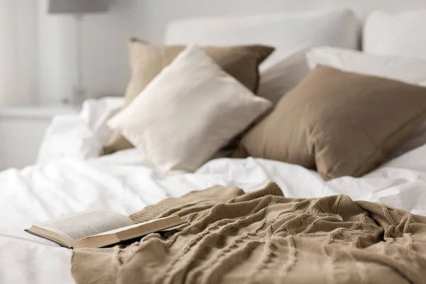 Cama con almohadas, manta y libro abierto en casa —  Fotos de Stock