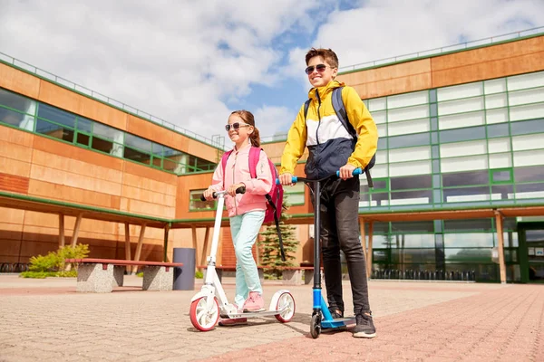 Gelukkige schoolkinderen met rugzakken en scooters — Stockfoto