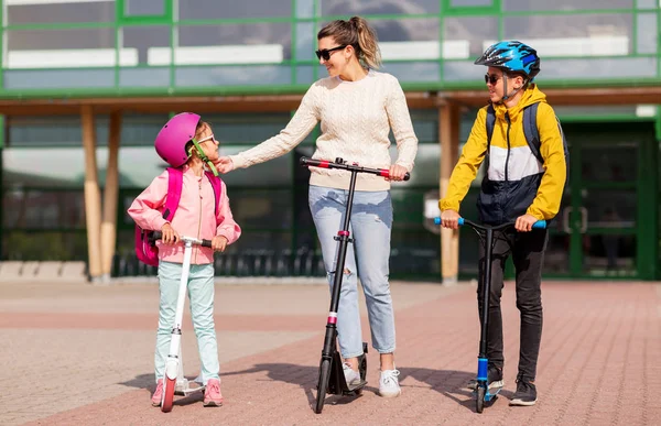 Gelukkig schoolkinderen met moeder paardrijden scooters — Stockfoto