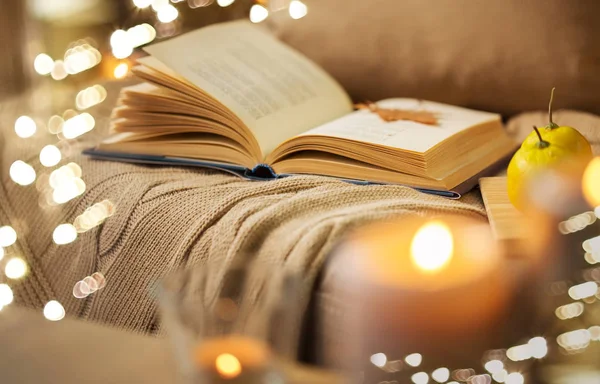 Livro com folha de outono e cobertor no sofá em casa — Fotografia de Stock