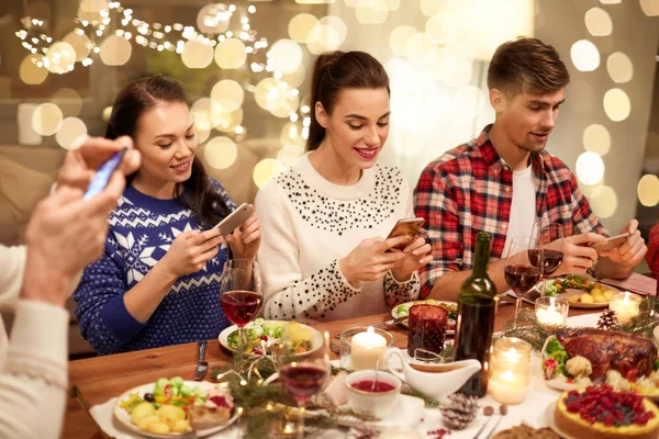 Friends with smartphones having christmas dinner — Stock Photo, Image