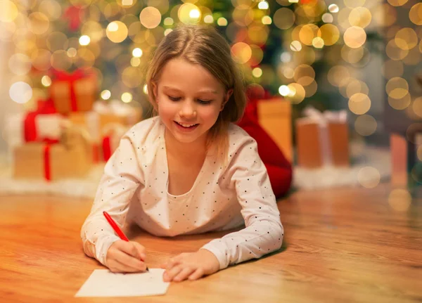 Sorridente ragazza scrittura lista dei desideri di Natale a casa — Foto Stock