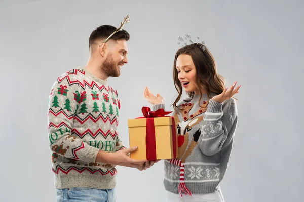Счастливая пара в рождественских свитерах с подарочной коробкой — стоковое фото