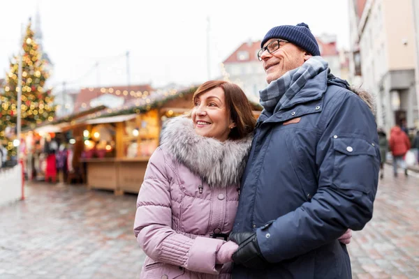 Счастливая пожилая пара обнимается на рождественском рынке — стоковое фото