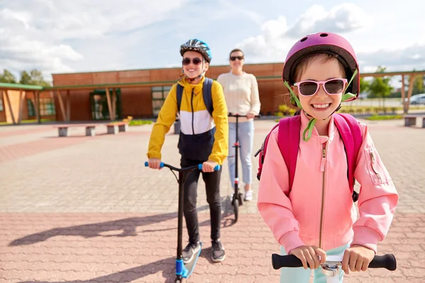 Gelukkig schoolkinderen met moeder paardrijden scooters — Stockfoto