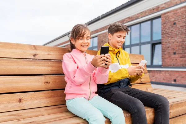 Barn med smartphones sitter på gatbänk — Stockfoto