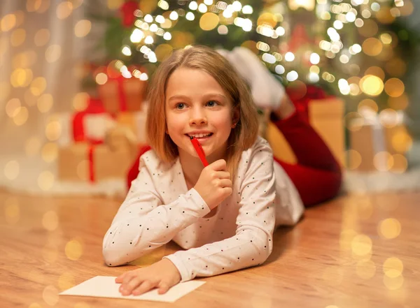 自宅でクリスマスの買い物リストを書いている女の子を笑顔 — ストック写真