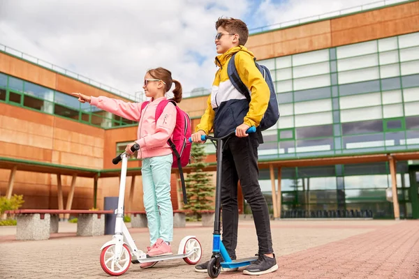 Gelukkige schoolkinderen met rugzakken en scooters — Stockfoto