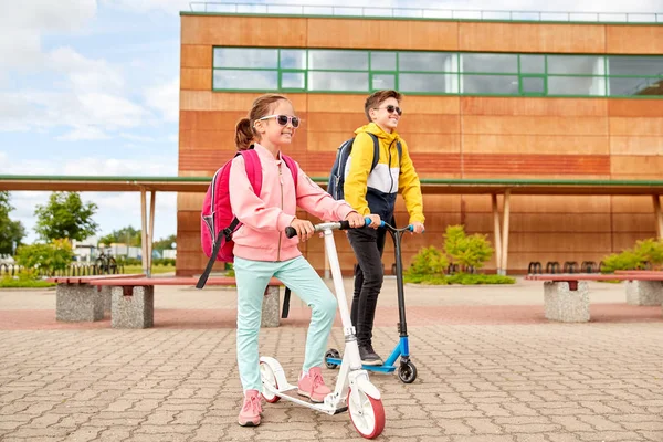 Niños de escuela feliz con mochilas y scooters —  Fotos de Stock