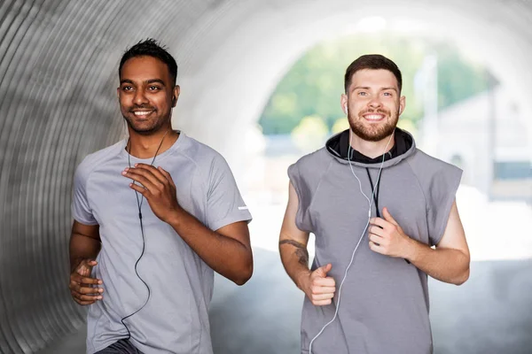 Male friends with earphones running outdoors — Stock Photo, Image