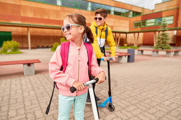 Crianças da escola feliz com mochilas e scooters — Fotografia de Stock