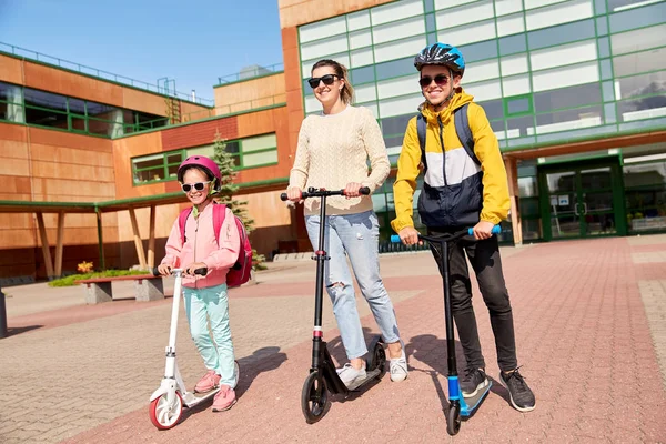 Gelukkig schoolkinderen met moeder paardrijden scooters — Stockfoto