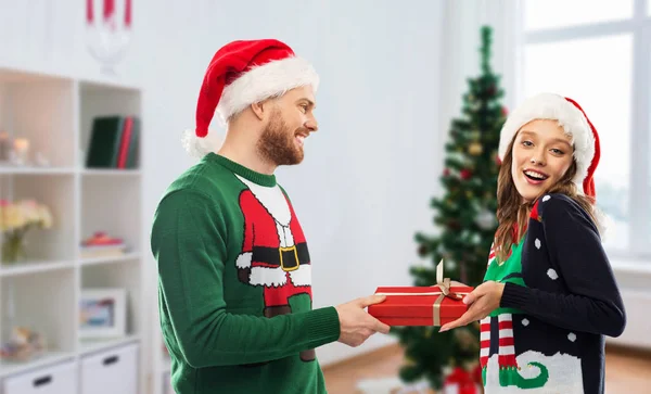 Šťastný pár v ošklivých svetrů s vánočním dárkem — Stock fotografie