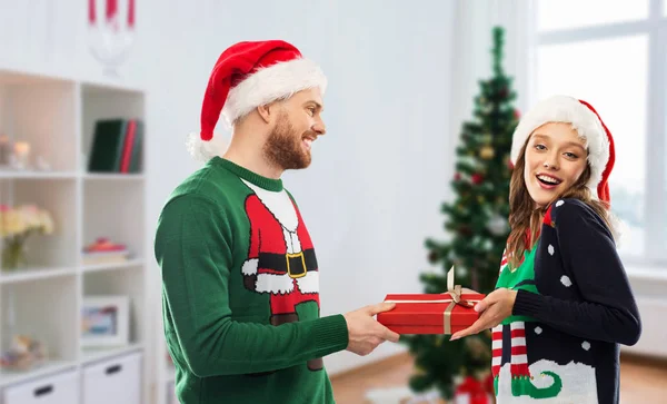 Casal feliz em camisolas feias com presente de Natal — Fotografia de Stock