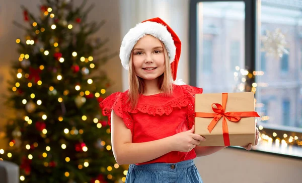 Noel Baba şapkalı kız Noel hediyesiyle evde. — Stok fotoğraf