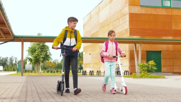 Niños de escuela feliz con mochilas y scooters — Vídeo de stock