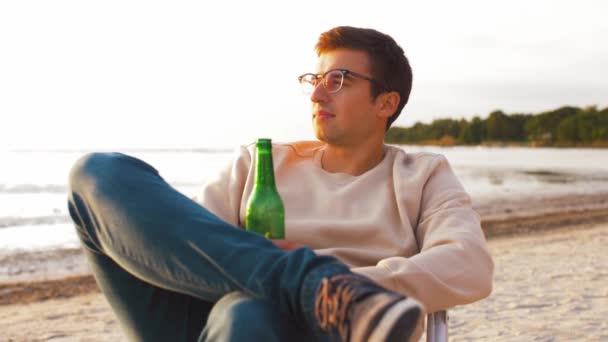 Man drinking beer sitting on chair on beach — Stock Video
